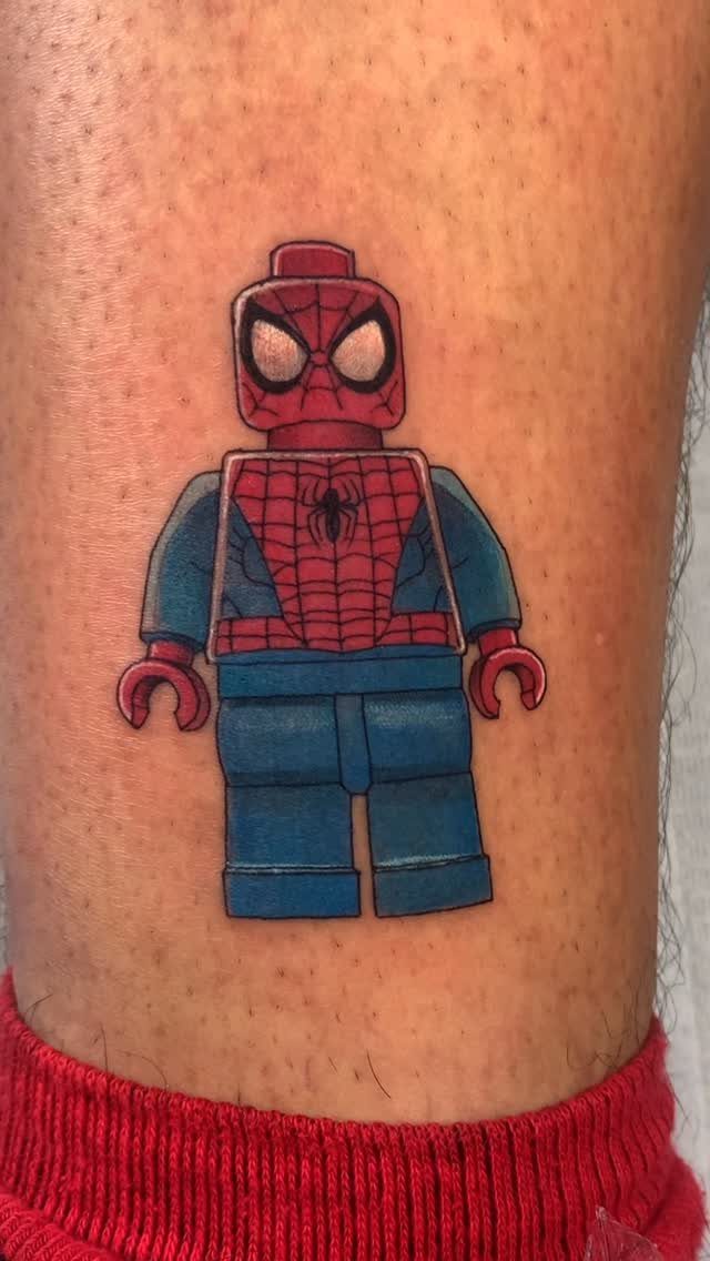 Lego Spider-Man minifigure tattoo on a person's arm with vibrant red and blue ink