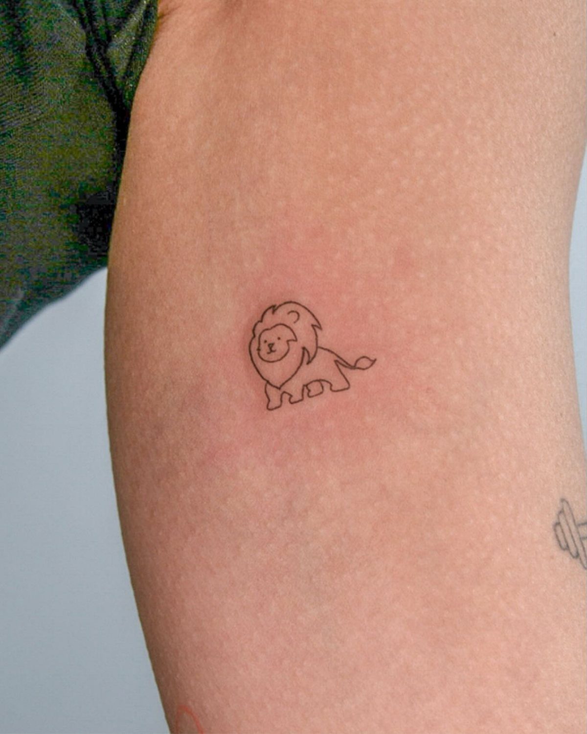 Small minimalist lion tattoo with clean black lines on a person's arm