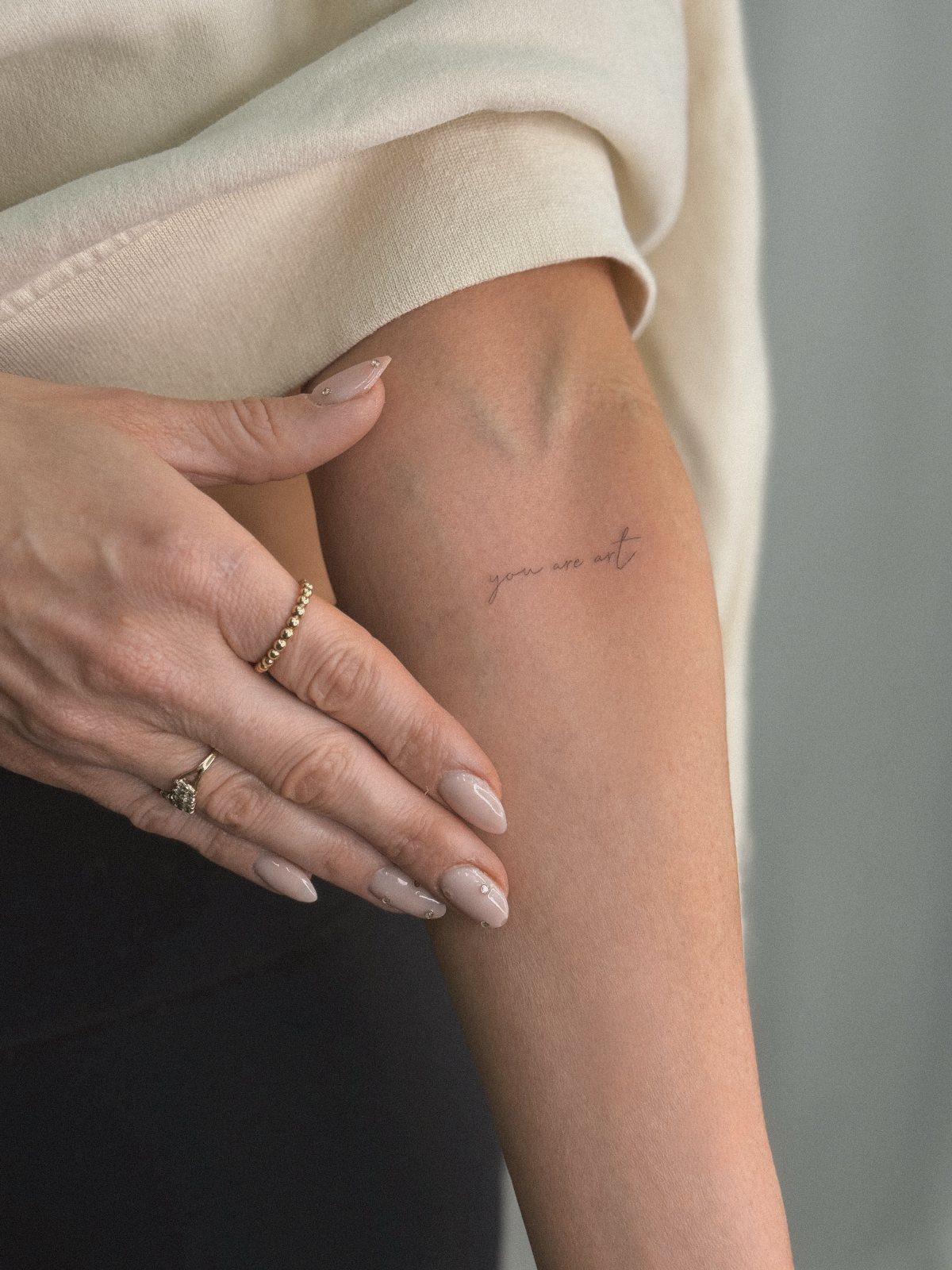 Cursive text tattoo reading you are art on a person's forearm