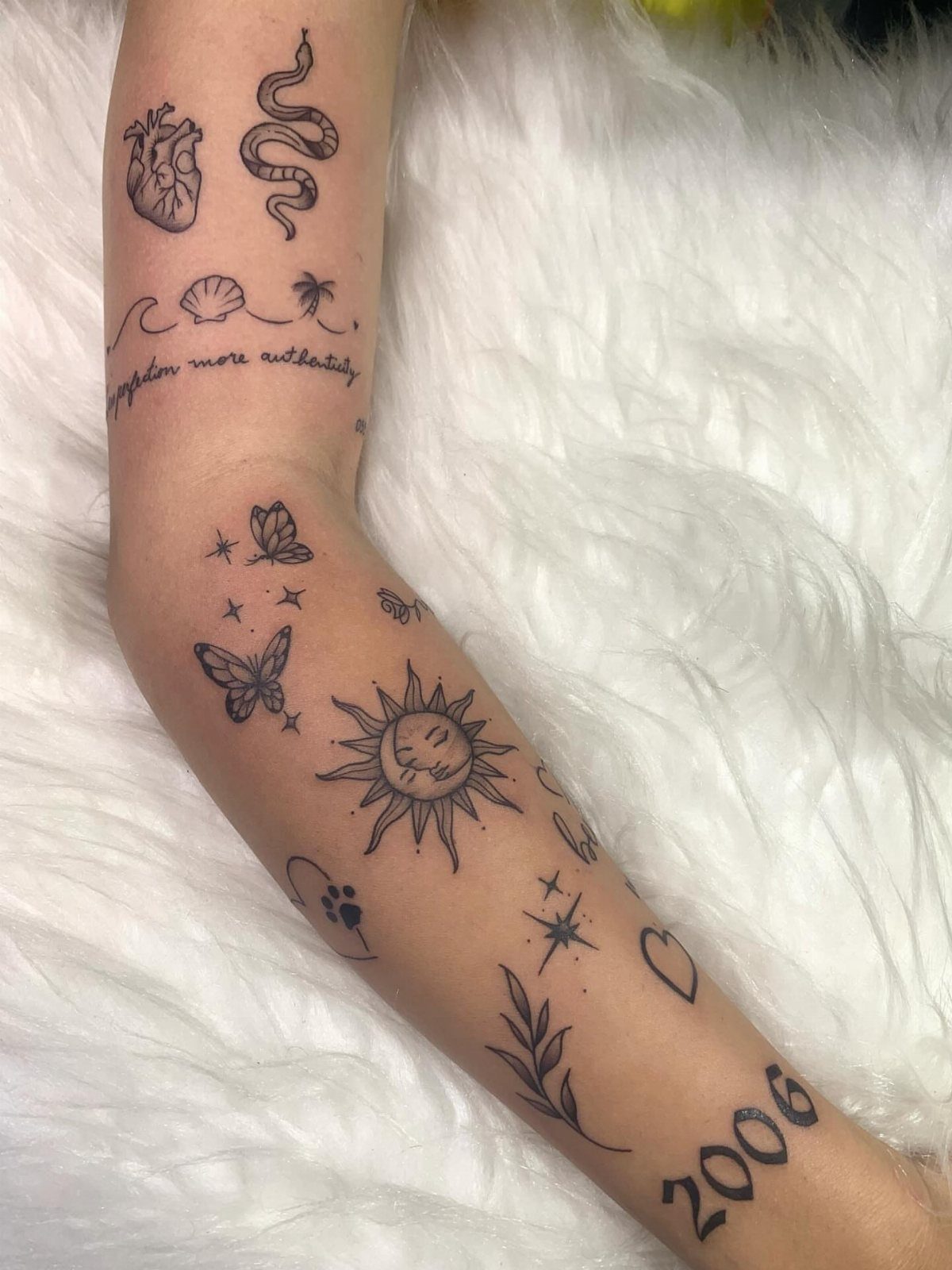 Arm with various small black ink tattoos including a sun, butterflies, and a snake.