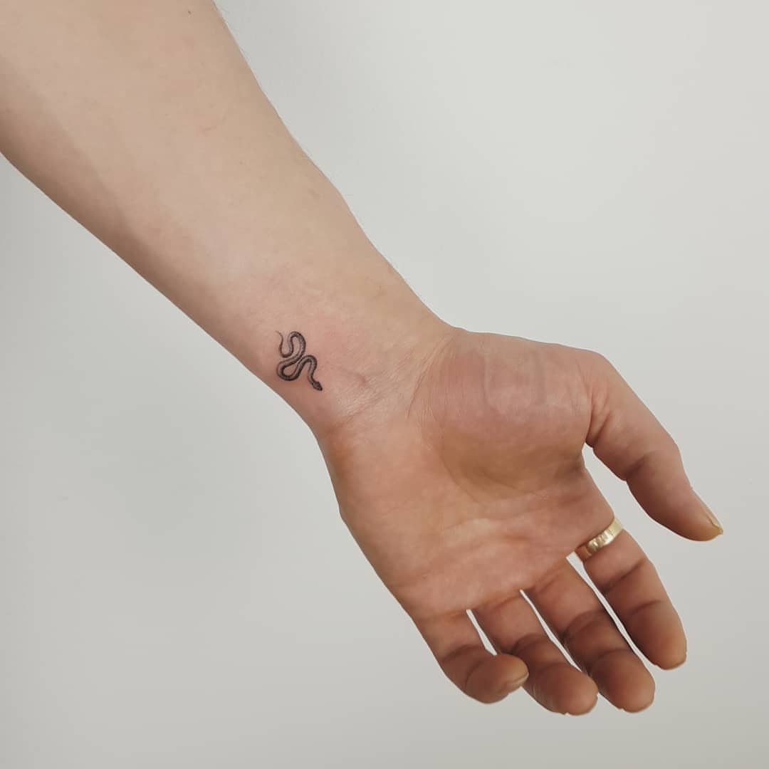 Small black snake tattoo on a person's inner wrist and hand.