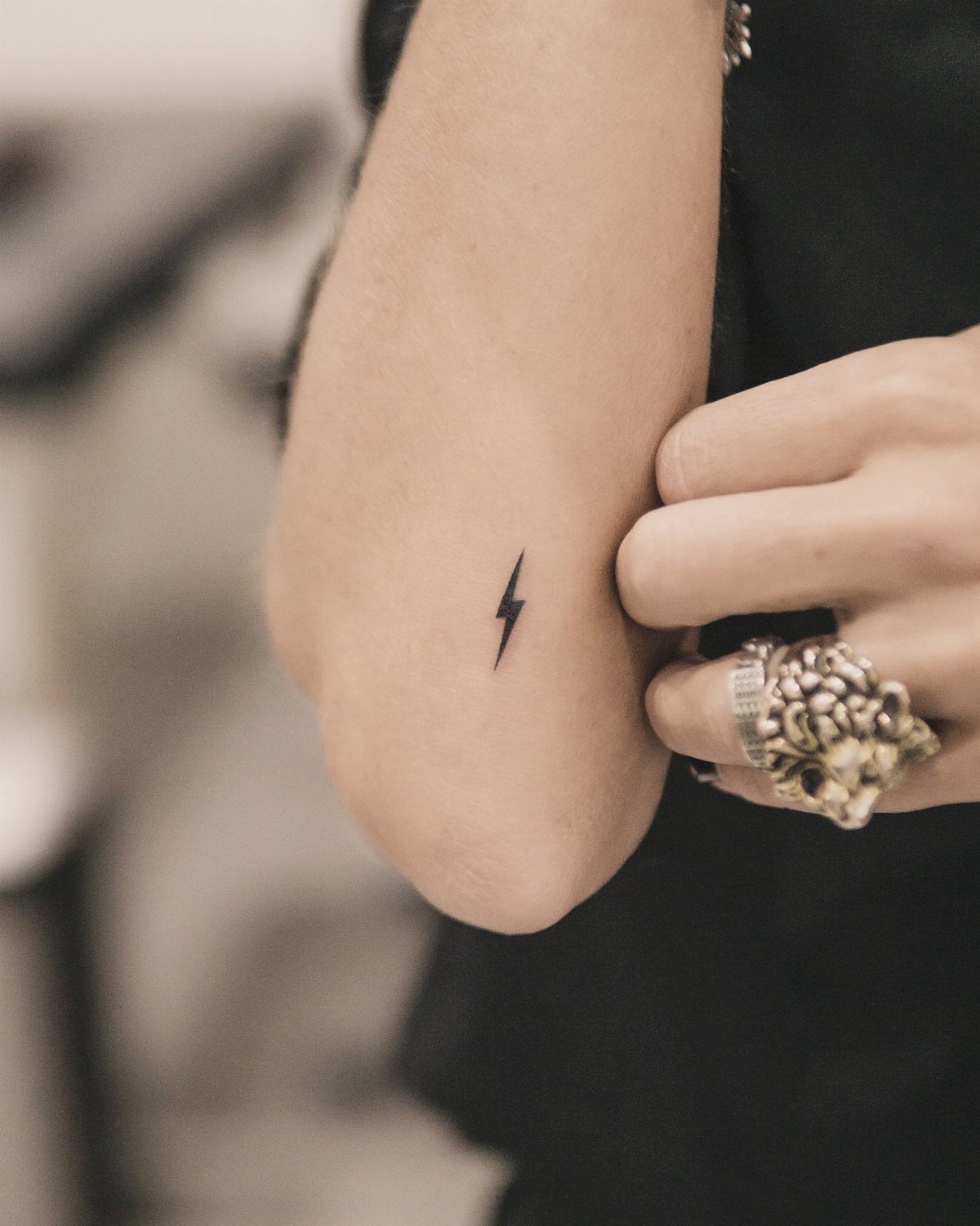 Small black lightning bolt tattoo on a person's inner forearm with silver ring.