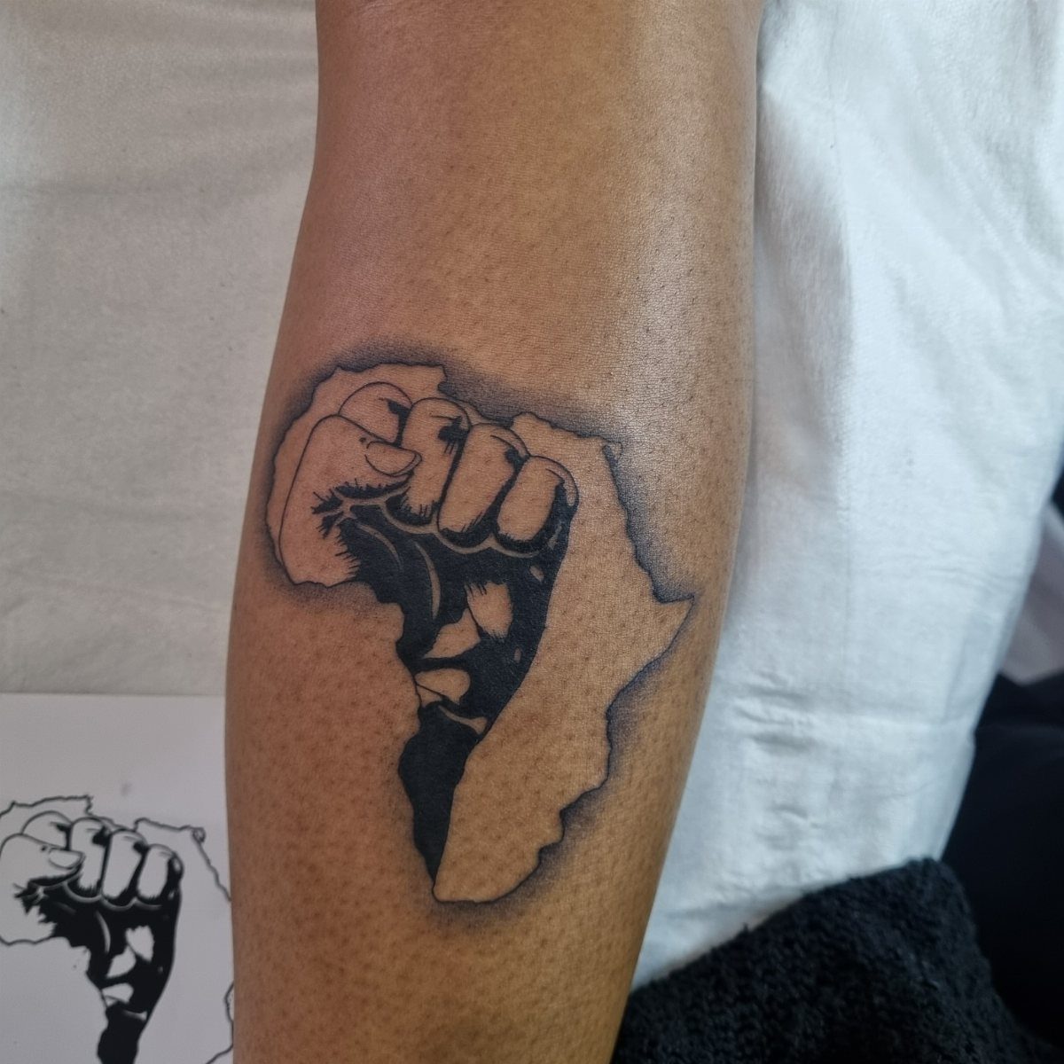 Tattoo of a clenched fist merged with the map of Africa on an arm