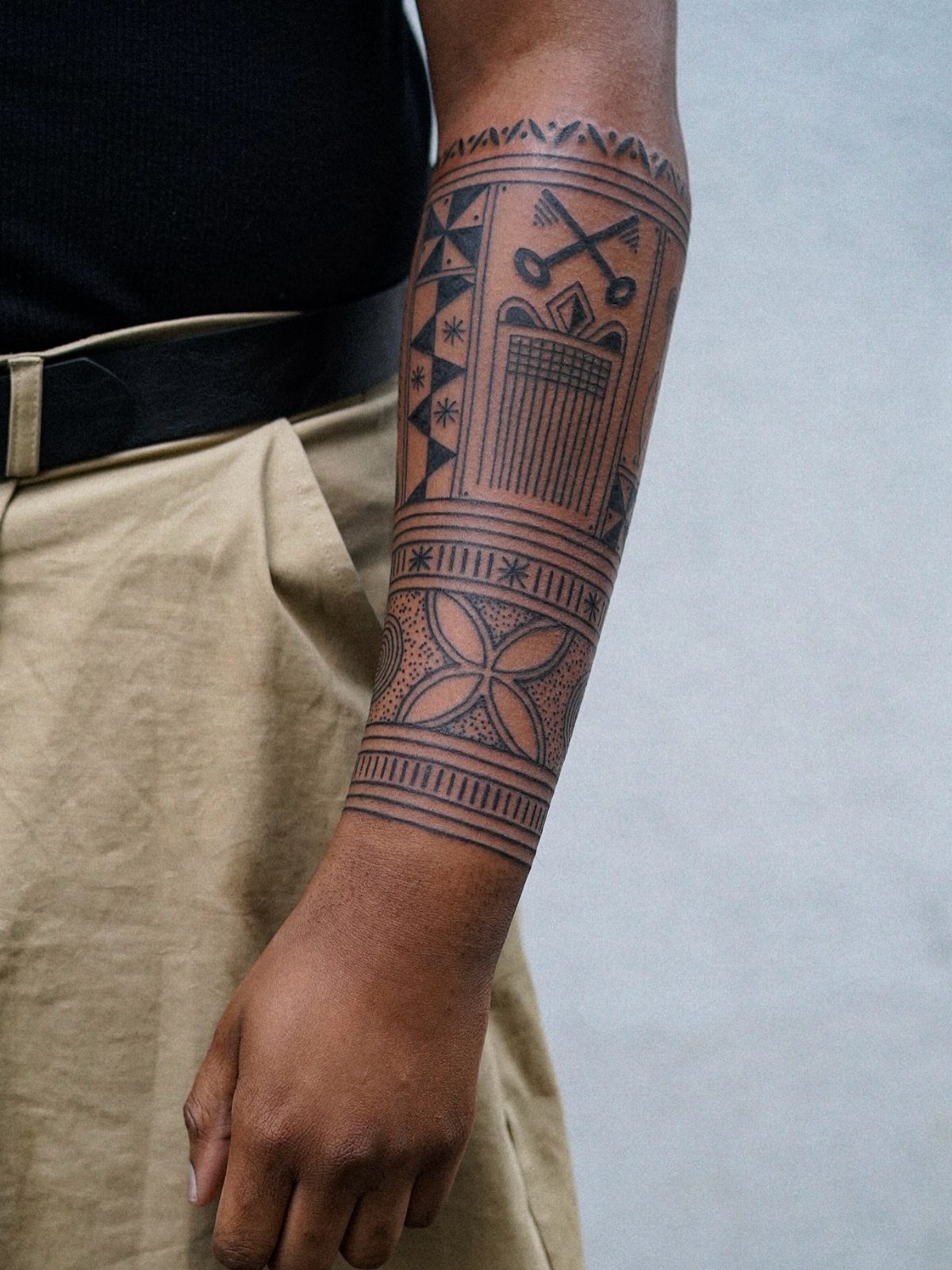 Forearm with a black ink tribal tattoo featuring geometric patterns and symbols.