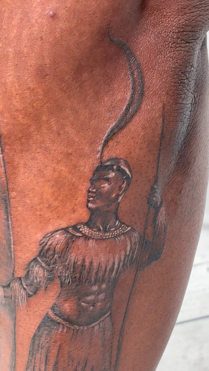 Zulu warrior tattoo on brown skin featuring traditional clothing and a spear