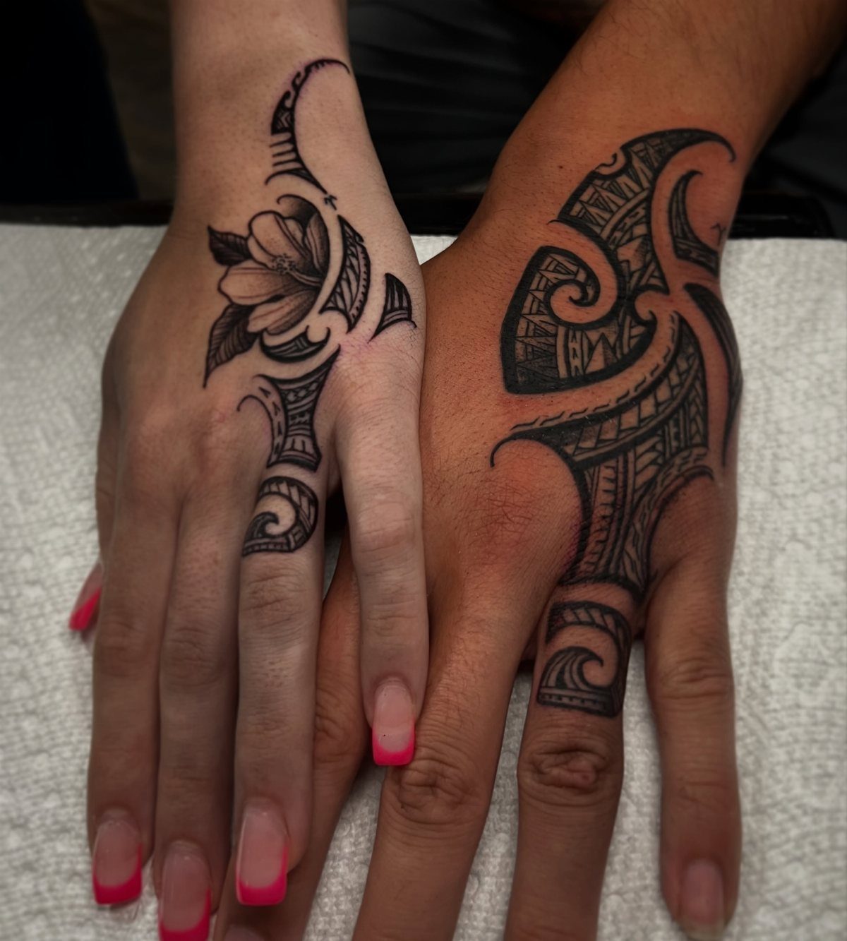 Tribal tattoos on the backs of two hands with black ink geometric patterns.