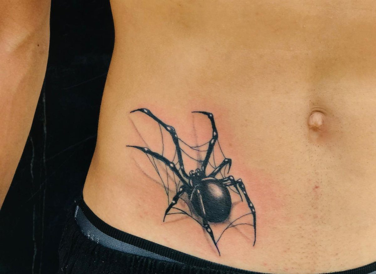 Black spider tattoo on a web located on a person's lower stomach area.