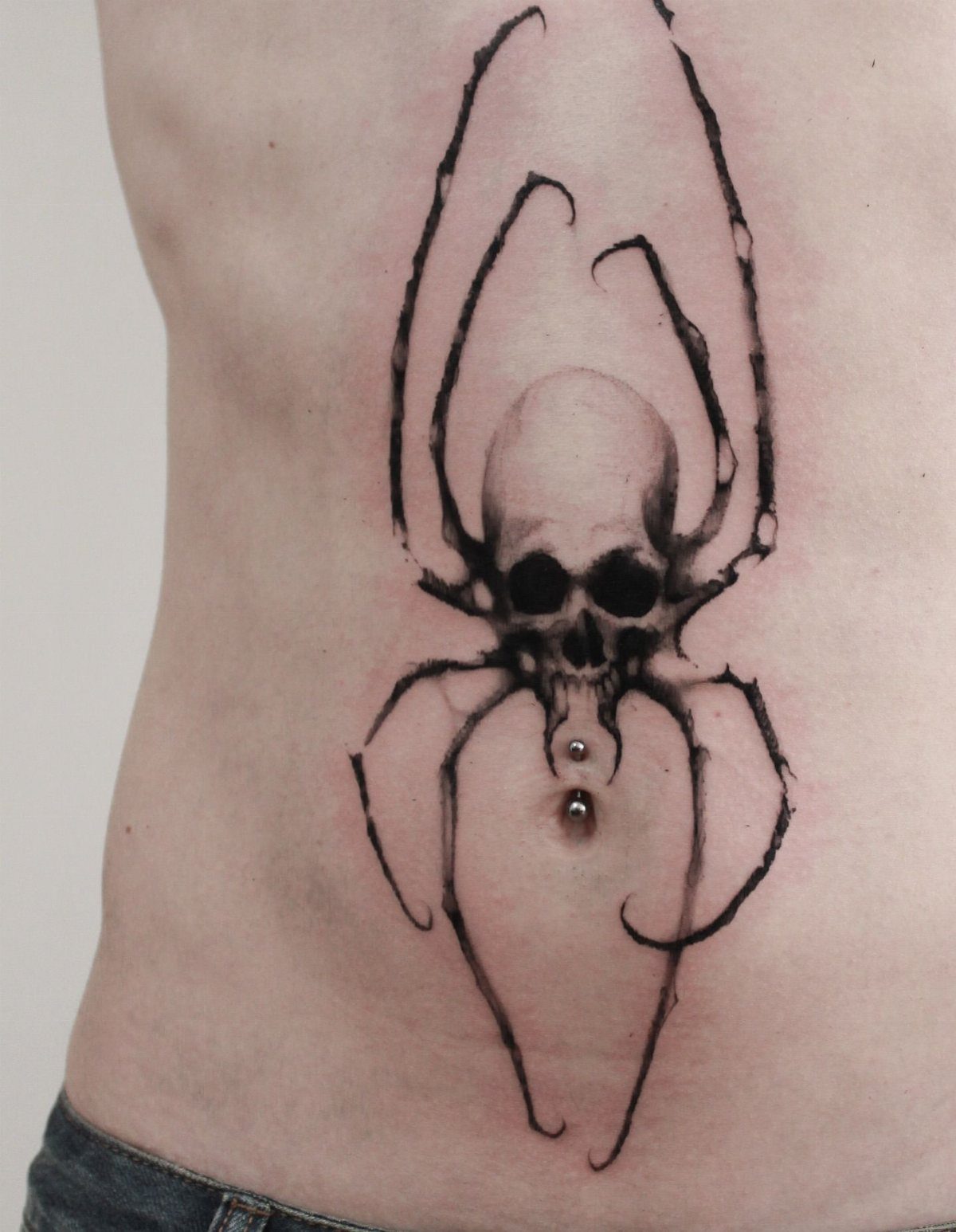 Skull with spider legs tattoo centered on a person's stomach around the navel.