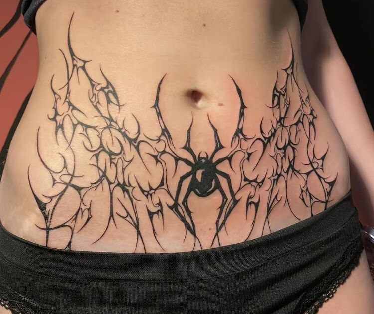 Spider tattoo with sharp black tribal patterns on a person's stomach.
