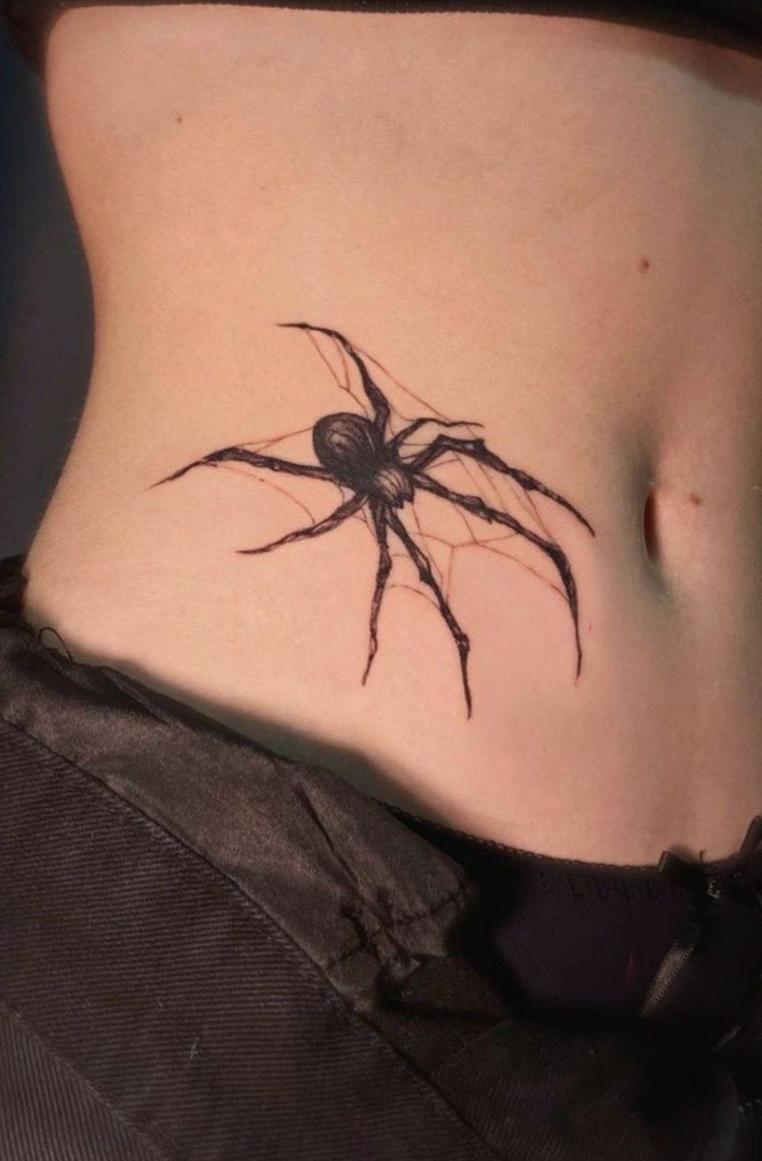 Spider on web tattoo on a person's stomach near the navel