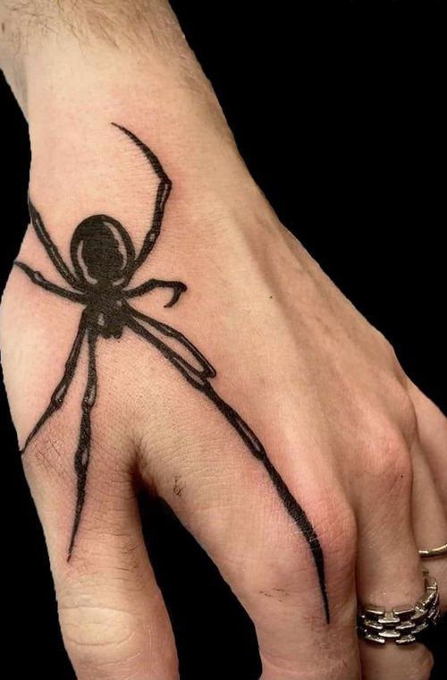 Black ink spider tattoo on the back of a hand with long legs.