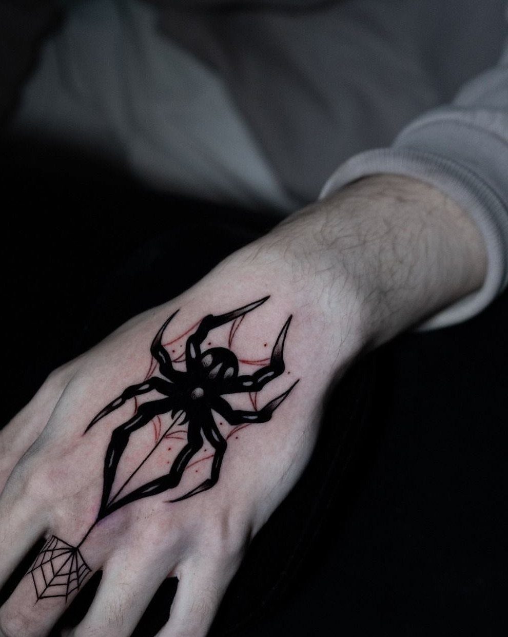 Geometric black spider tattoo with red details on the back of a hand