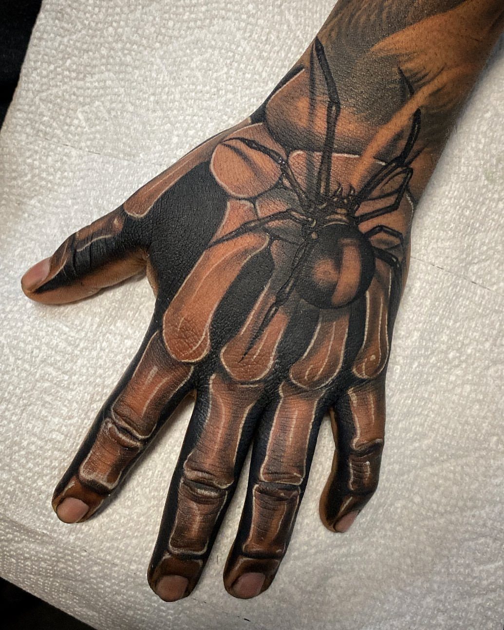 Realistic black ink spider tattoo on the back of a human hand
