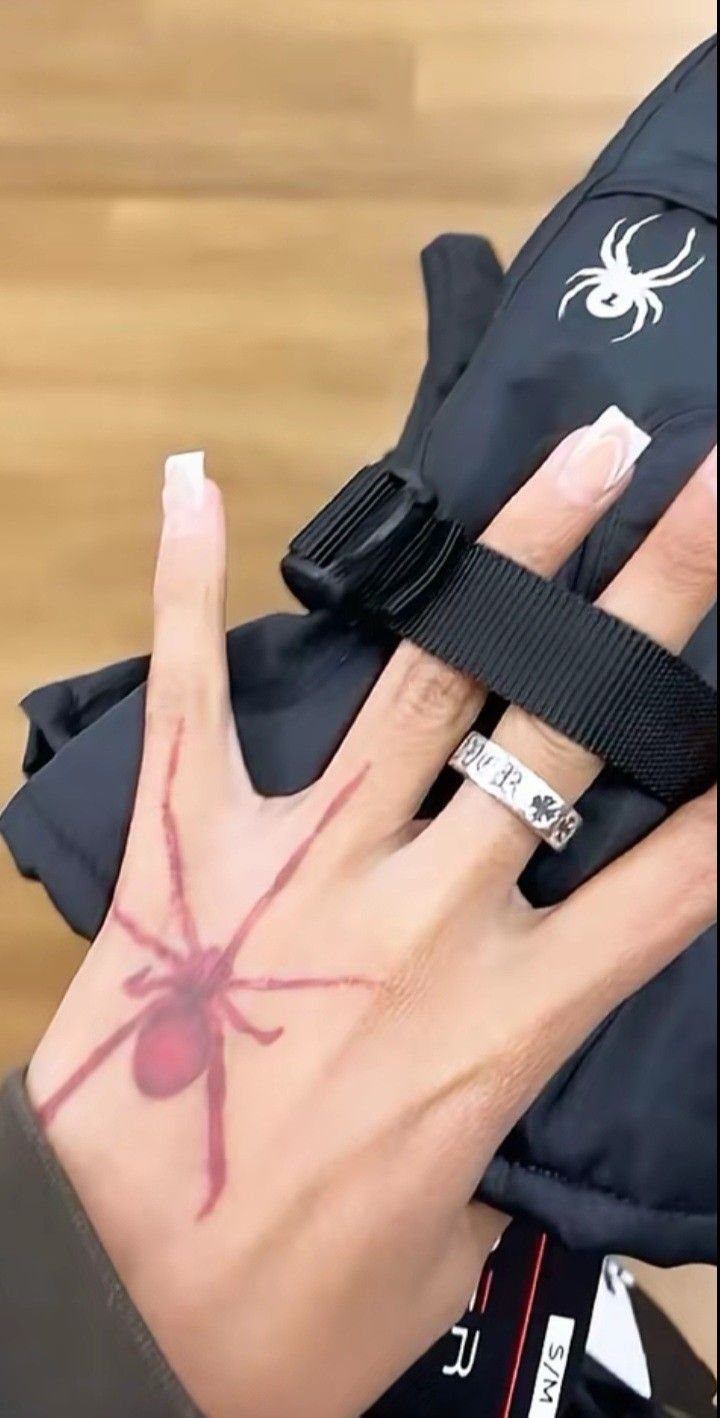 Red ink spider tattoo on the back of a person's hand