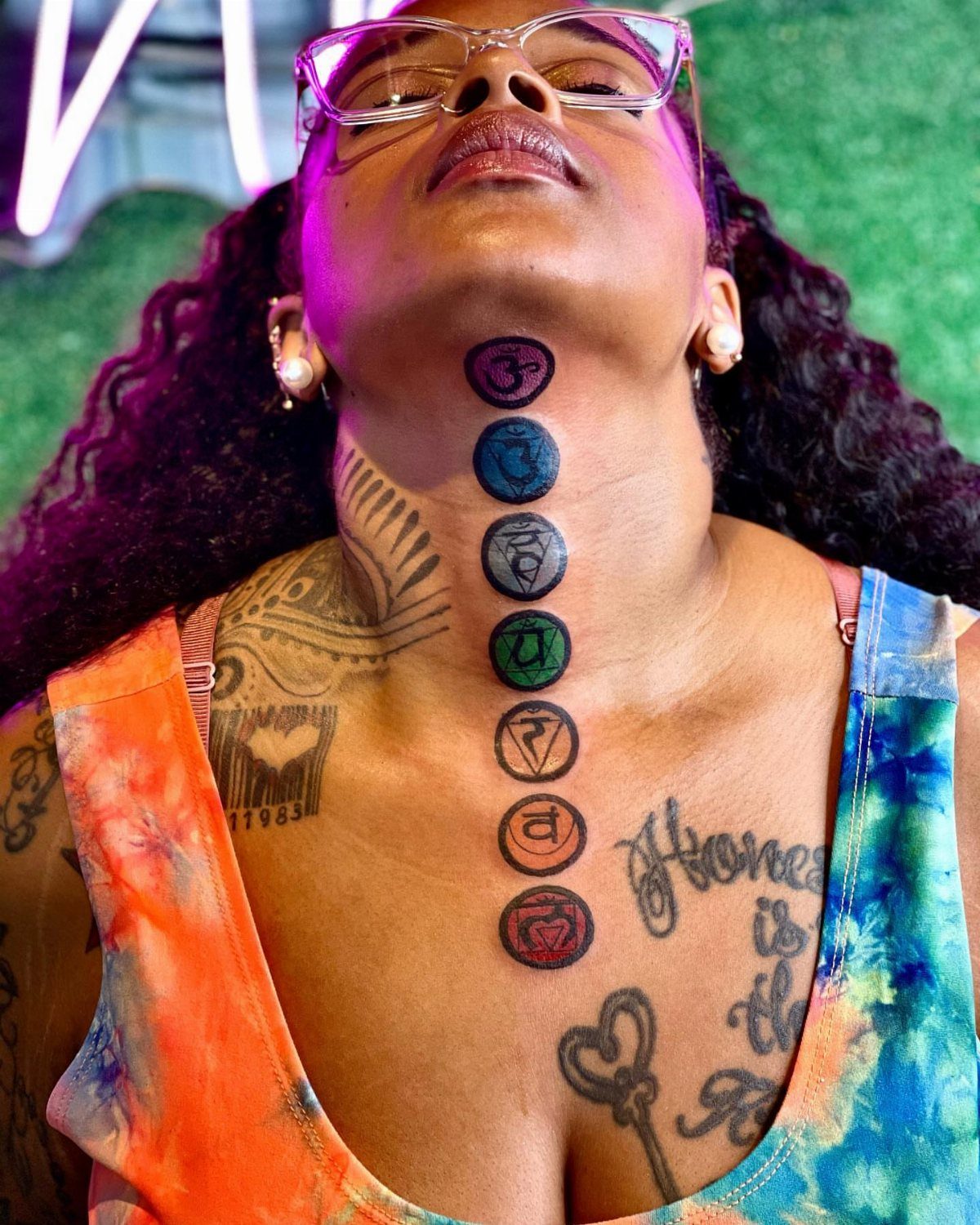Woman with a vertical row of seven colorful chakra symbol tattoos on her neck.