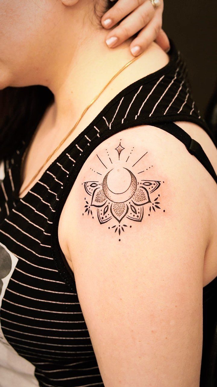 Crescent moon and lotus flower tattoo on a woman's shoulder in black ink.
