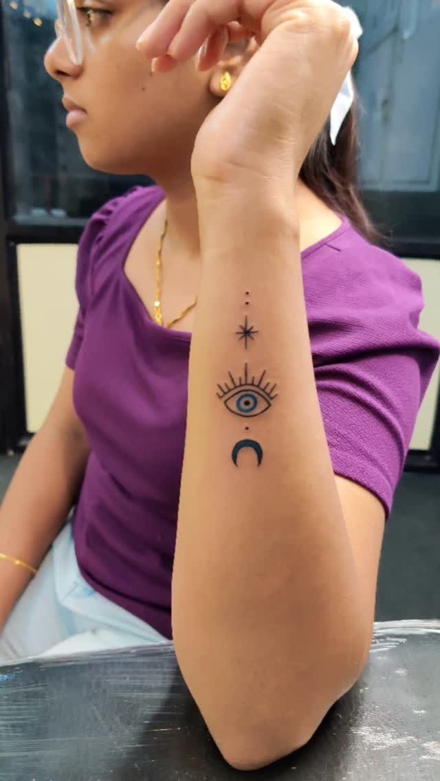 Forearm tattoo featuring a spiritual eye, crescent moon, and a small star.