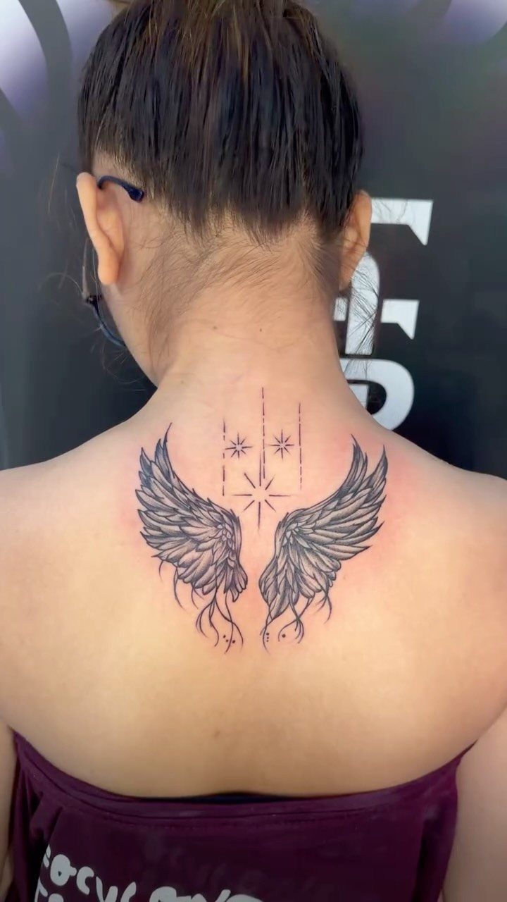 Angel wing tattoo on the upper back of a woman with a small star.