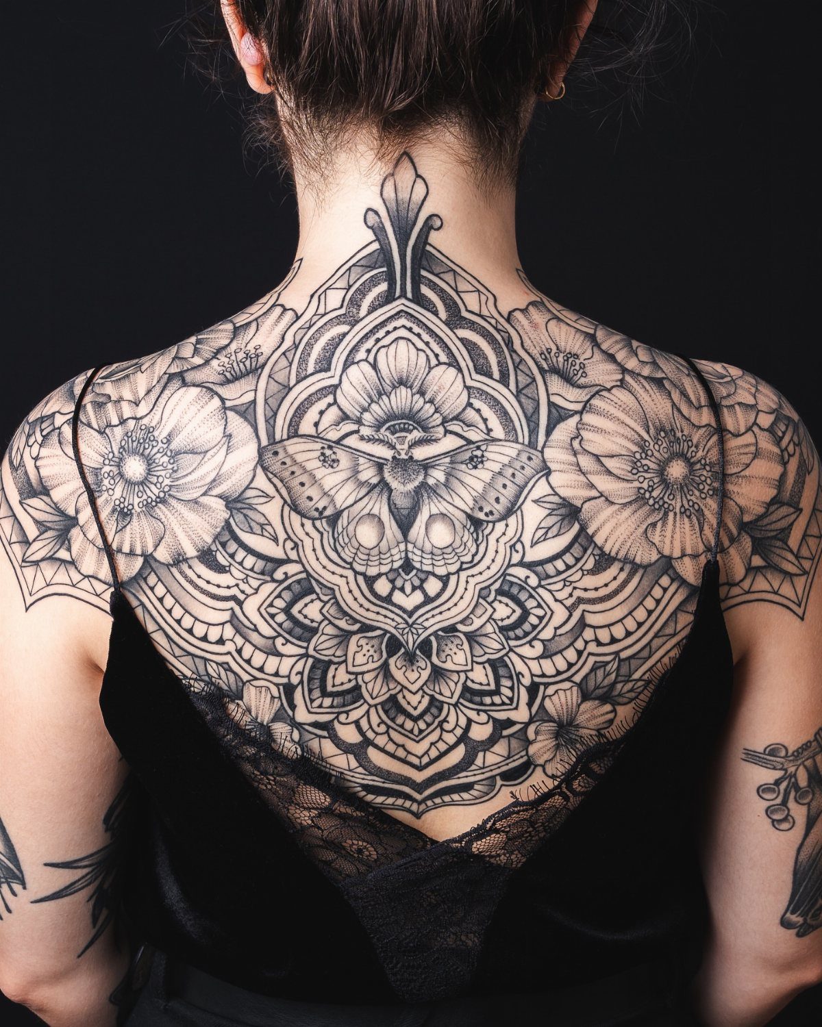 Intricate black ink mandala and moth tattoo on a woman's upper back