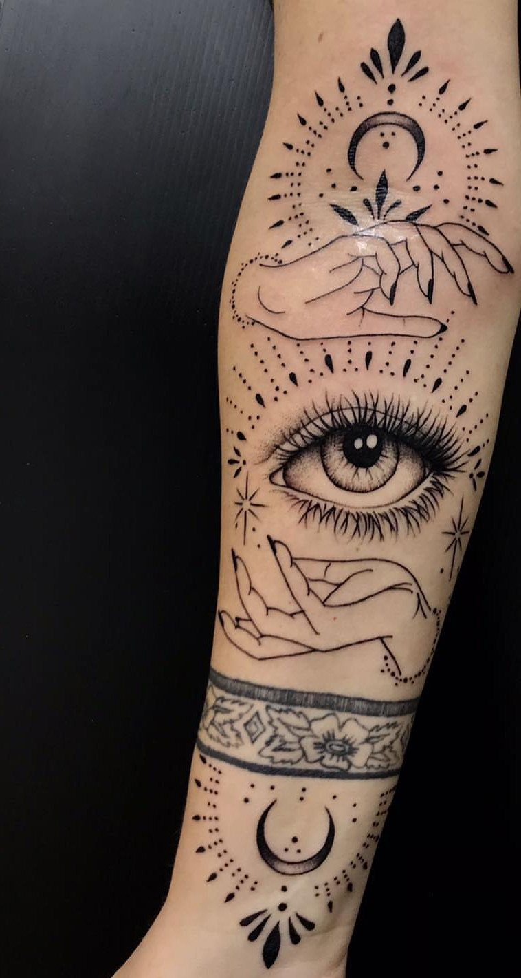 Spiritual eye tattoo on a forearm with hands, crescent moons, and celestial dots.