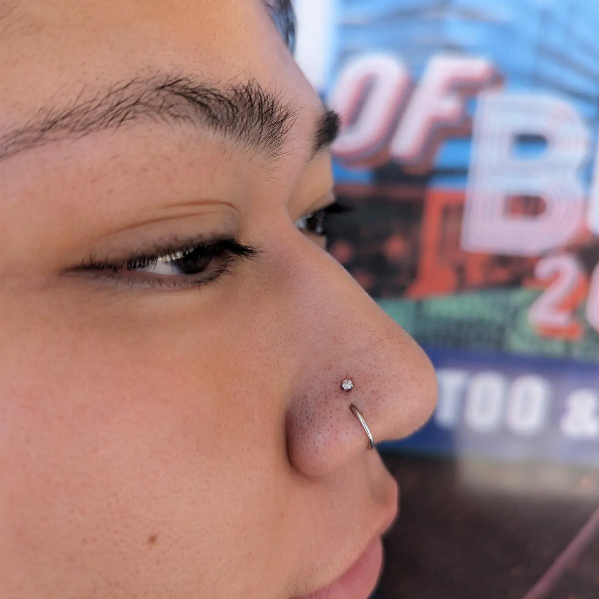 Person's nose with a stacked nostril piercing featuring a stud and a hoop.