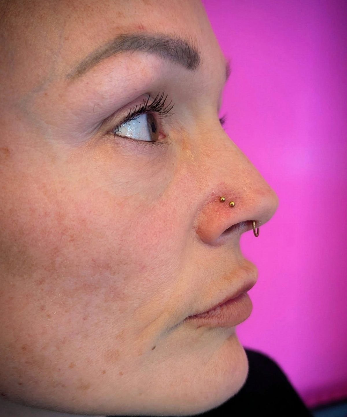 Person's profile featuring a stacked nose piercing with a gold stud and hoop.