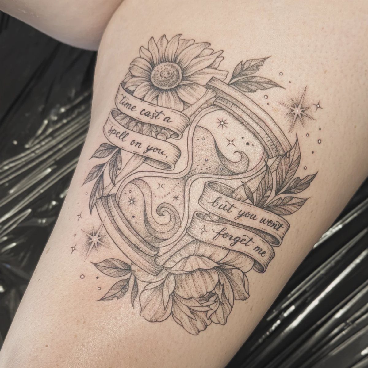 Hourglass tattoo with flowers and banners on a person's arm.