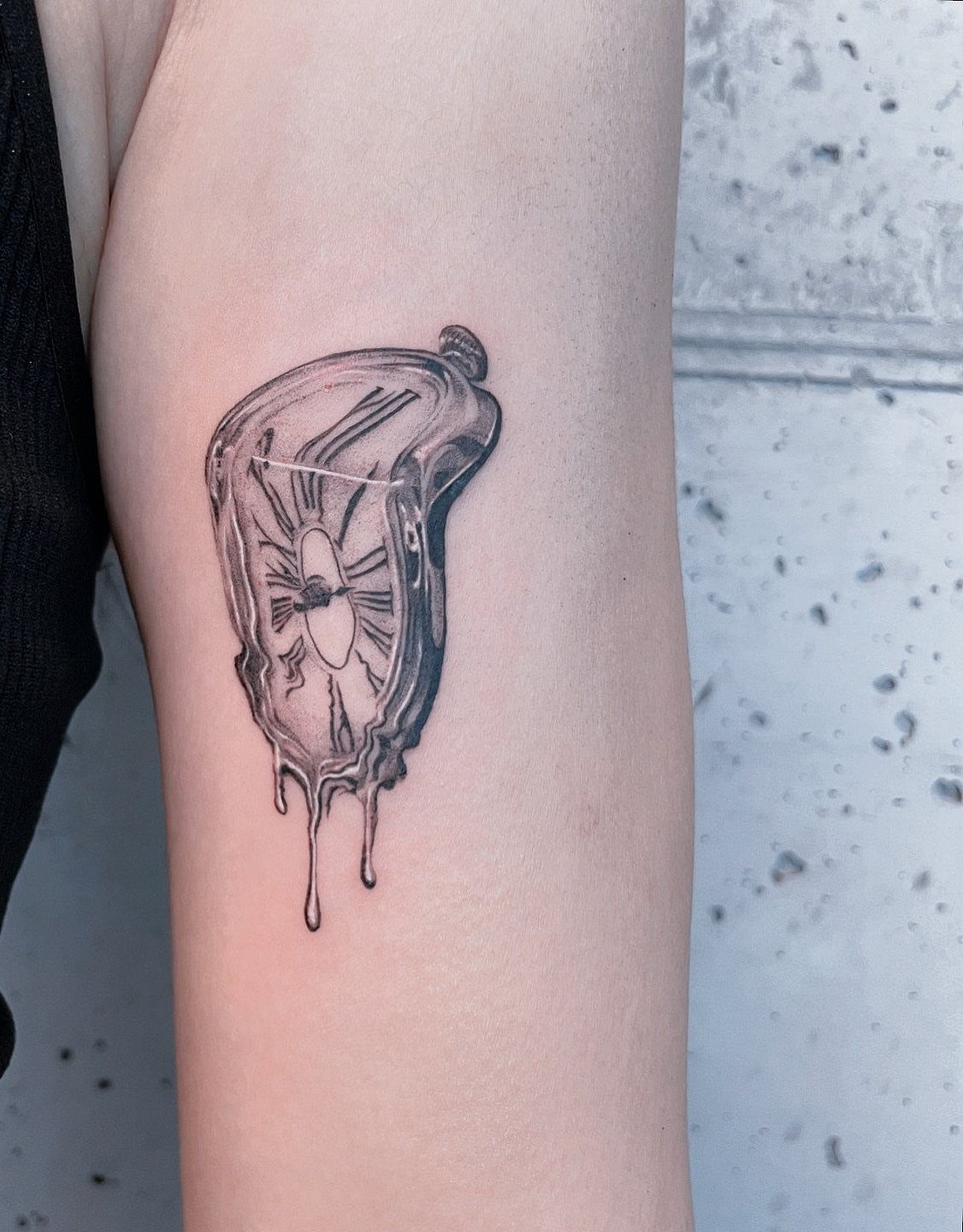 Melting clock tattoo with dripping edges on a person's upper arm.