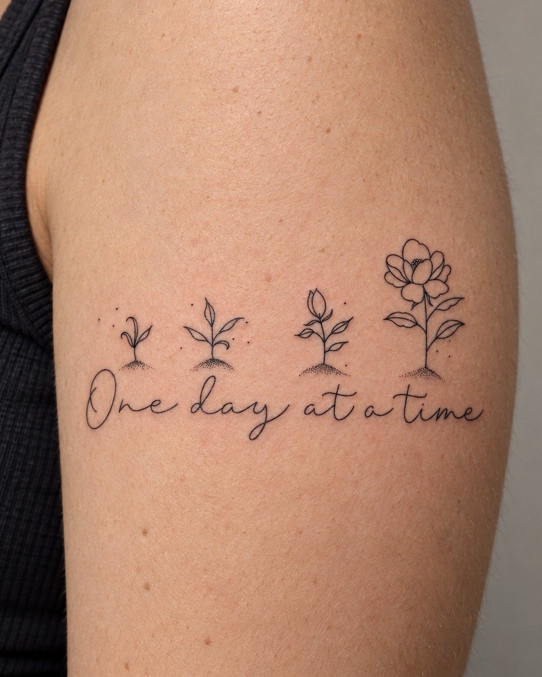 Tattoo on an arm with the words One day at a time and growing plants.