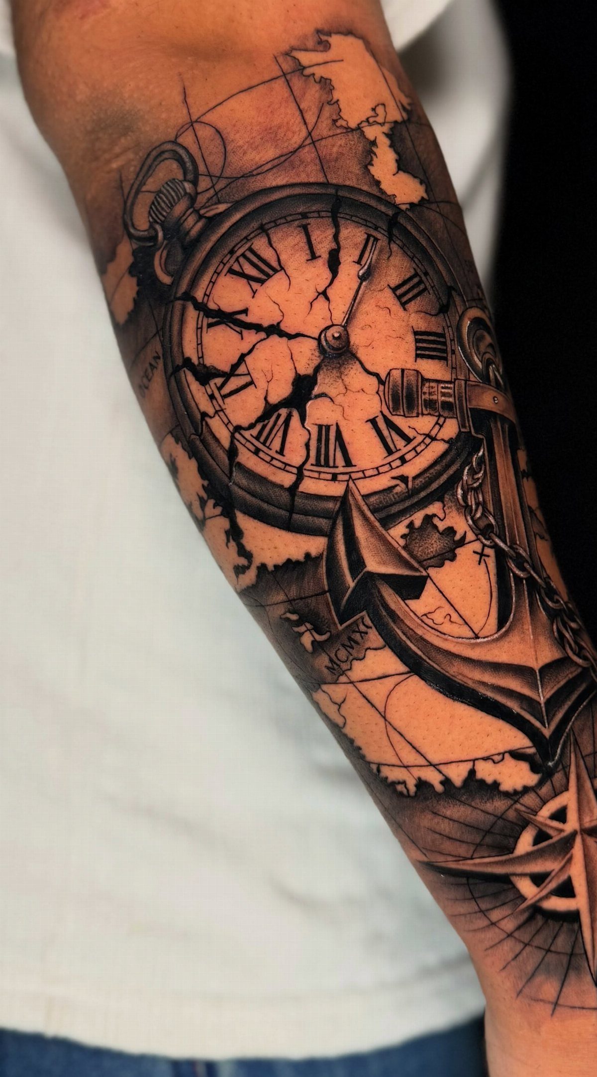 Pocket watch tattoo with a cracked face, anchor, and map on a forearm.