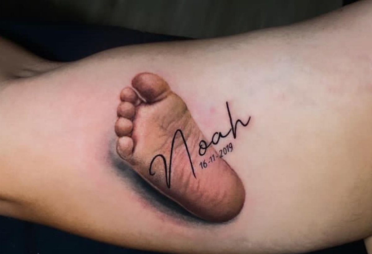 Realistic 3D baby foot tattoo on an arm with the name Noah written.