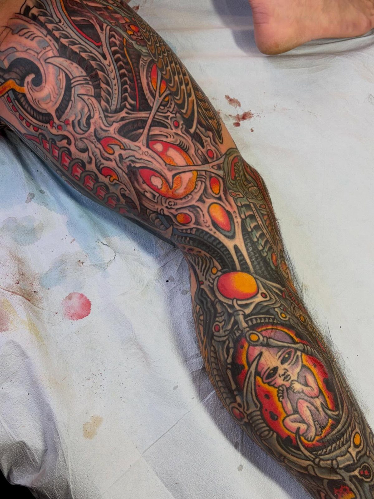 Biomechanical arm tattoo with grey mechanical parts and glowing orange circular details.