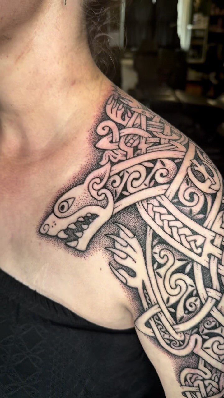 Celtic knotwork tattoo of a stylized wolf on a person's shoulder and arm.