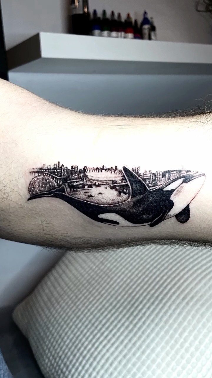 Orca whale and city skyline tattoo on a person's forearm in black ink