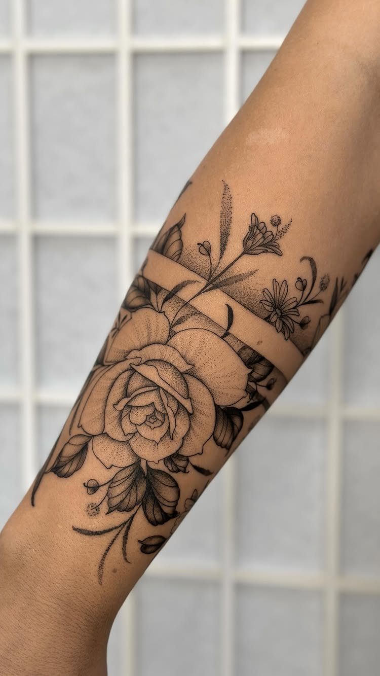 Floral tattoo with a rose and bands wrapping around a person's forearm.