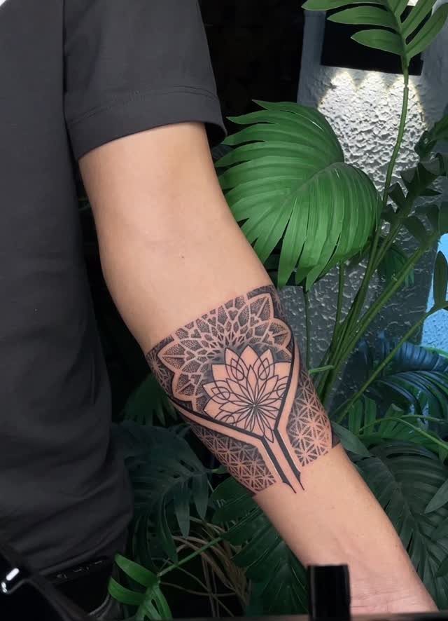 Geometric mandala tattoo on a person's forearm with green tropical leaves in background