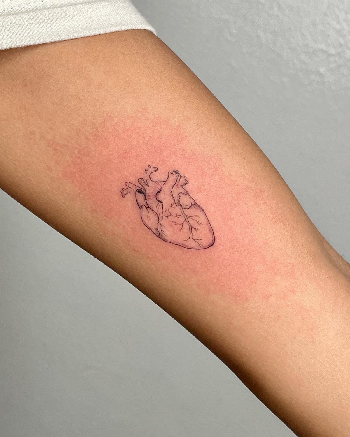 Anatomical heart tattoo in black ink on a person's forearm.