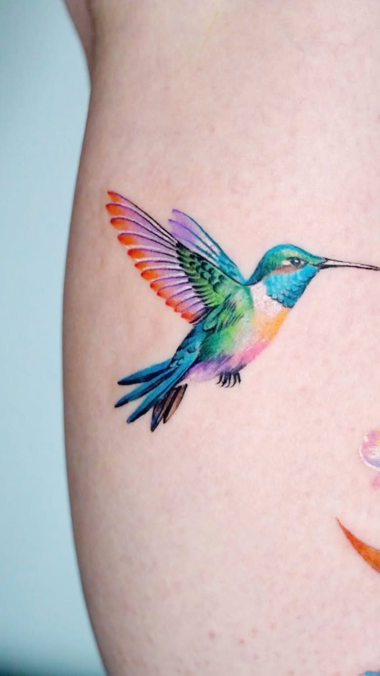 Colorful hummingbird tattoo with vibrant blue and green feathers on a person's arm.