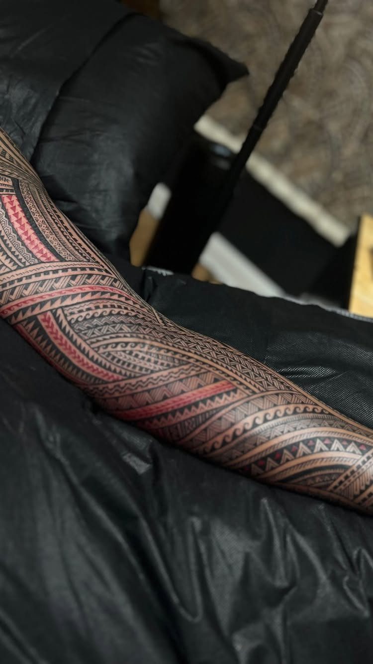 Polynesian sleeve tattoo with black and red geometric patterns on a person's arm.