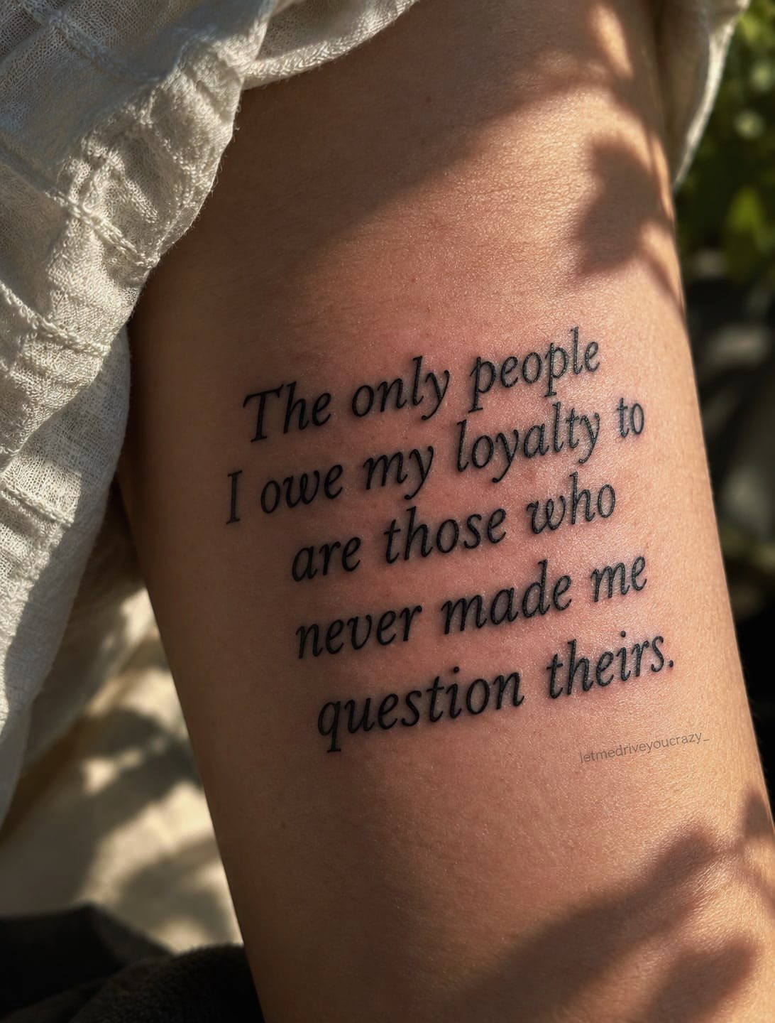 Black ink quote tattoo on a person's arm with a cursive serif font.