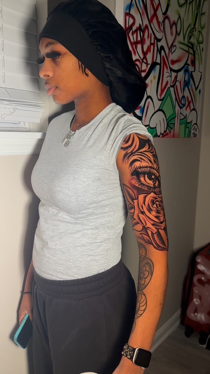 Woman with a half sleeve tattoo of a realistic eye and rose on her arm