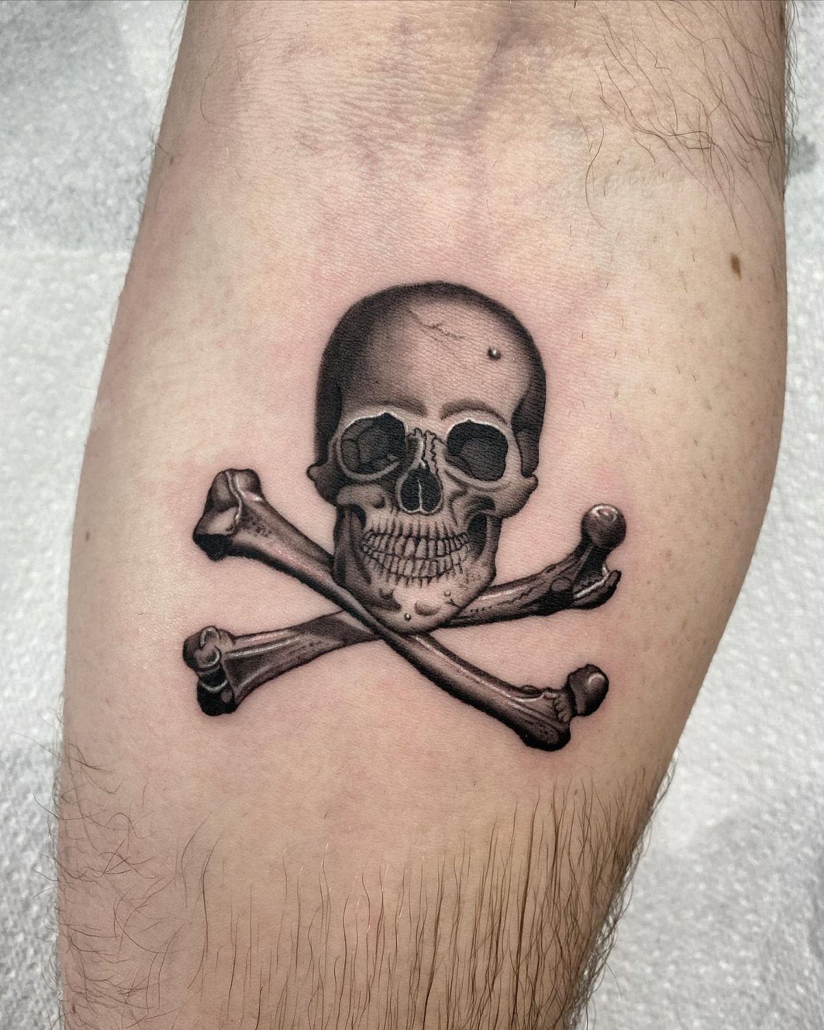 Skull and crossbones tattoo with realistic shading on a person's forearm
