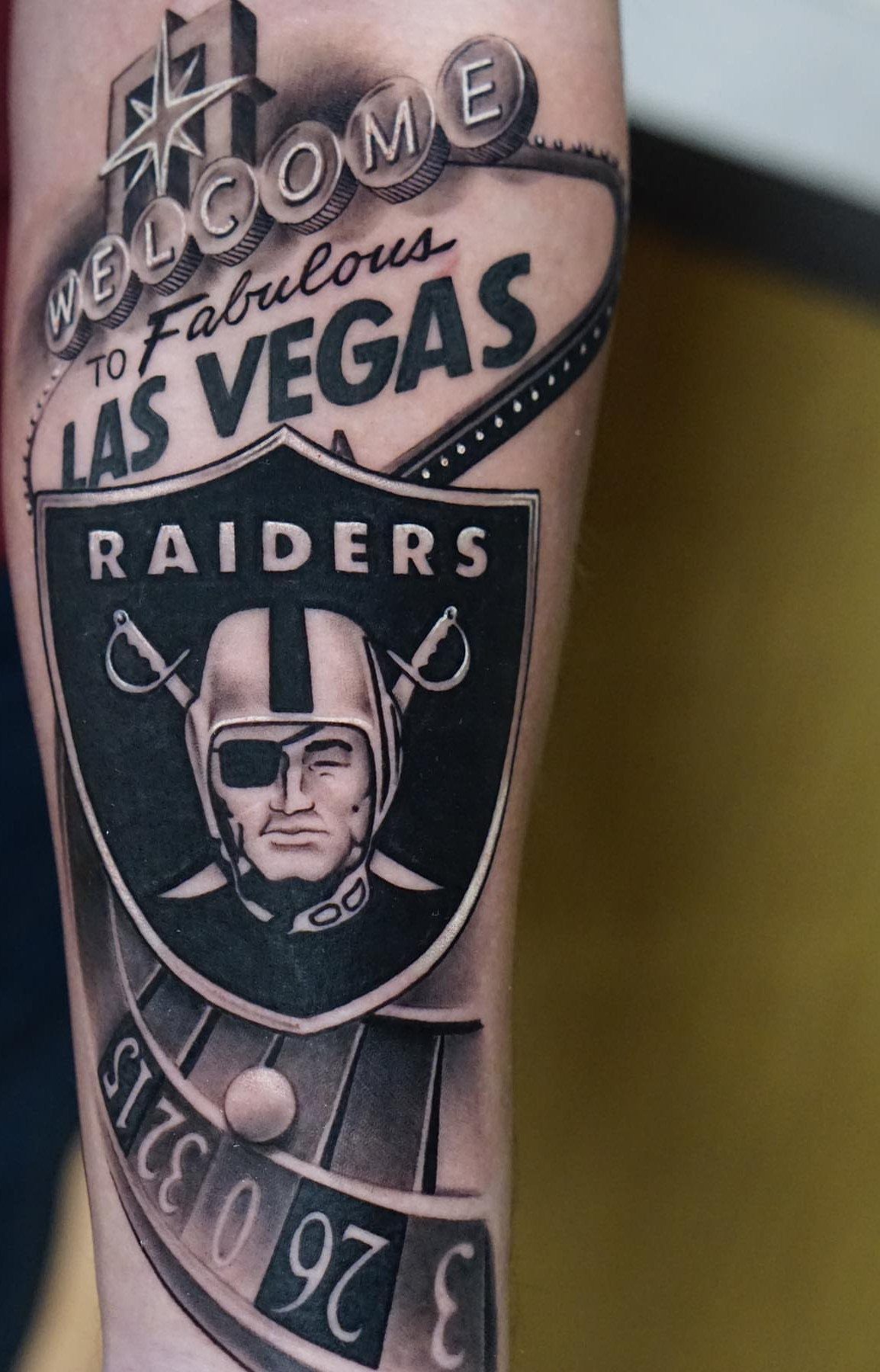 Las Vegas Raiders mascot tattoo on an arm with city signage and roulette wheel.