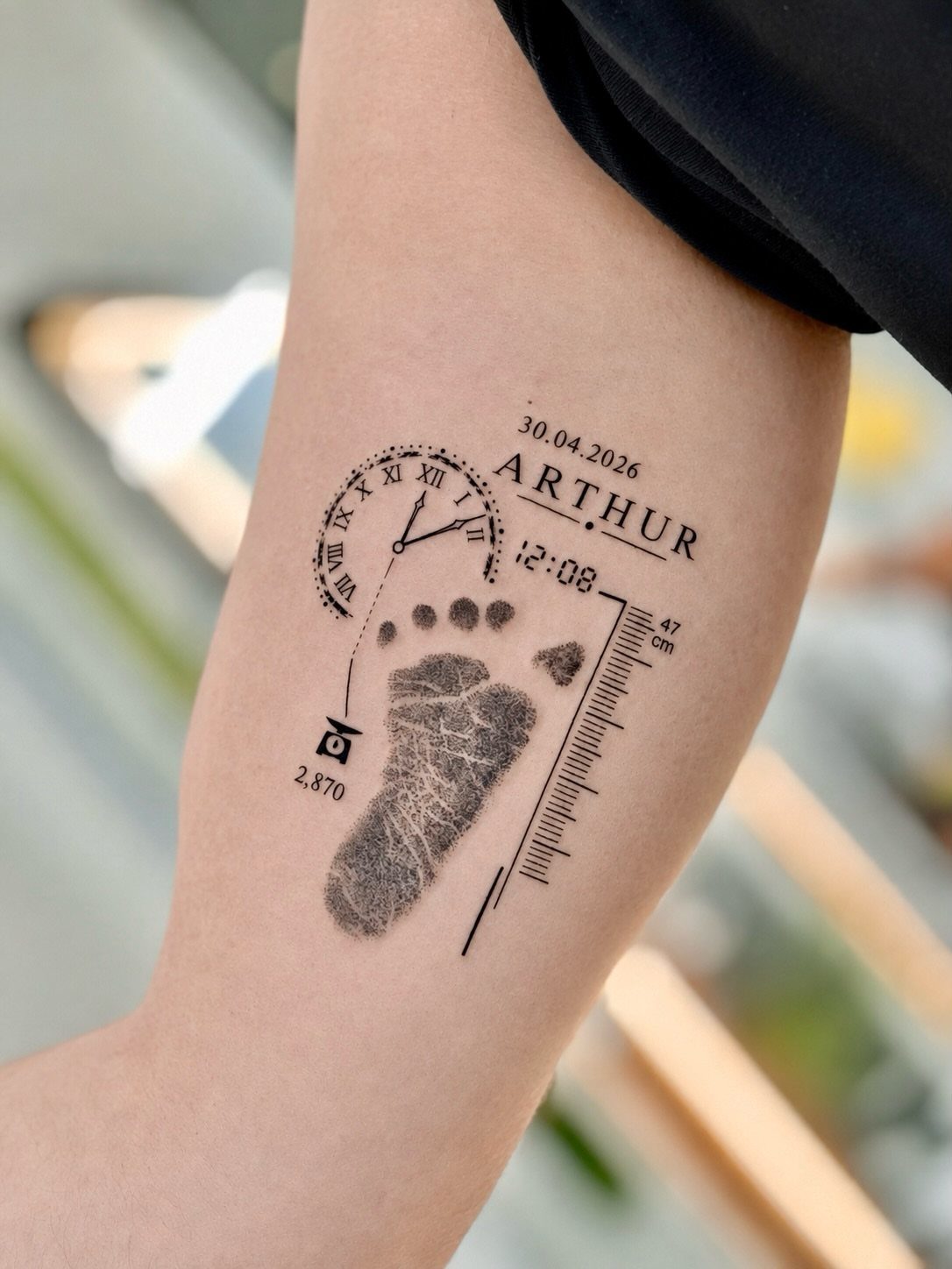 Forearm tattoo featuring a baby footprint, clock, name Arthur, and birth date.