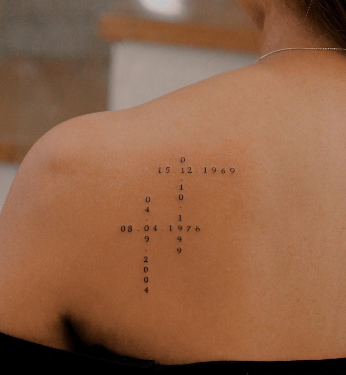 Tattoos of birth dates and years arranged in a cross on a shoulder.