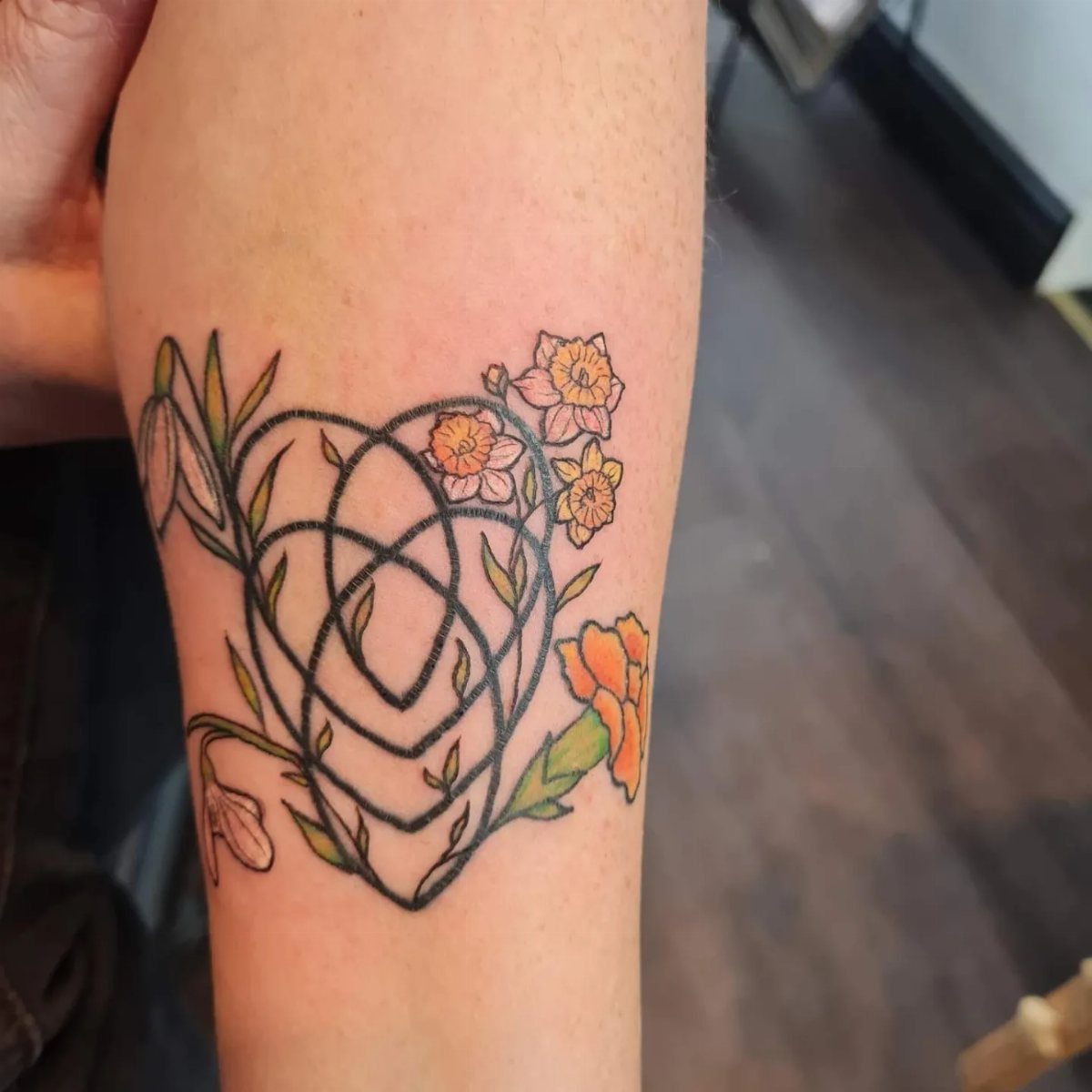 Celtic motherhood knot tattoo in a heart shape with orange and white flowers.