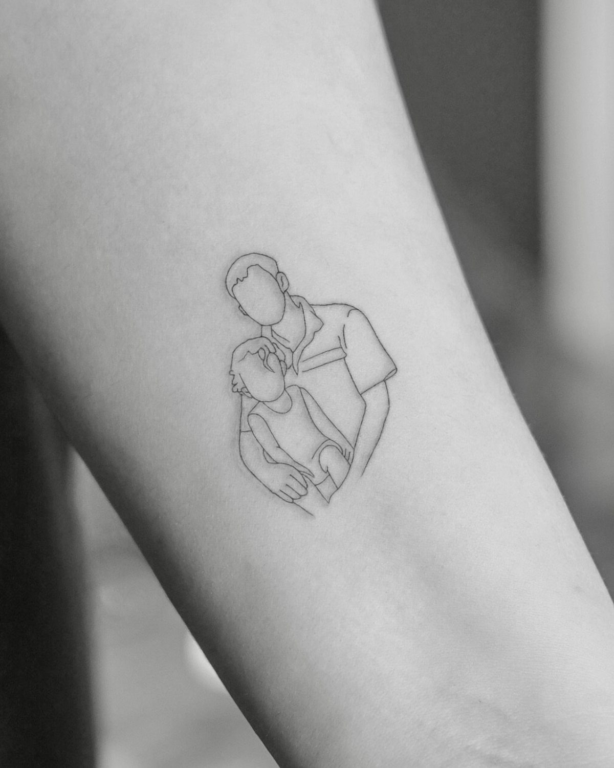 Minimalist fine-line tattoo of a parent holding a child on a forearm