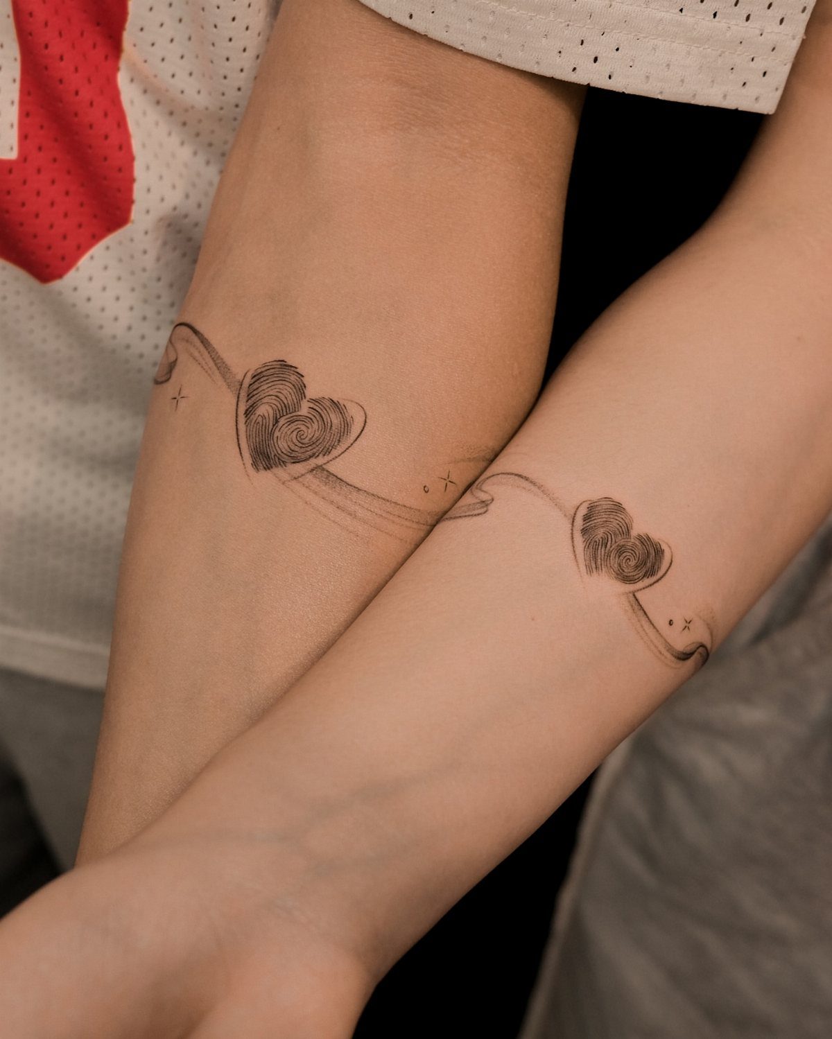 Matching fingerprint heart tattoos on two forearms with flowing wavy lines.