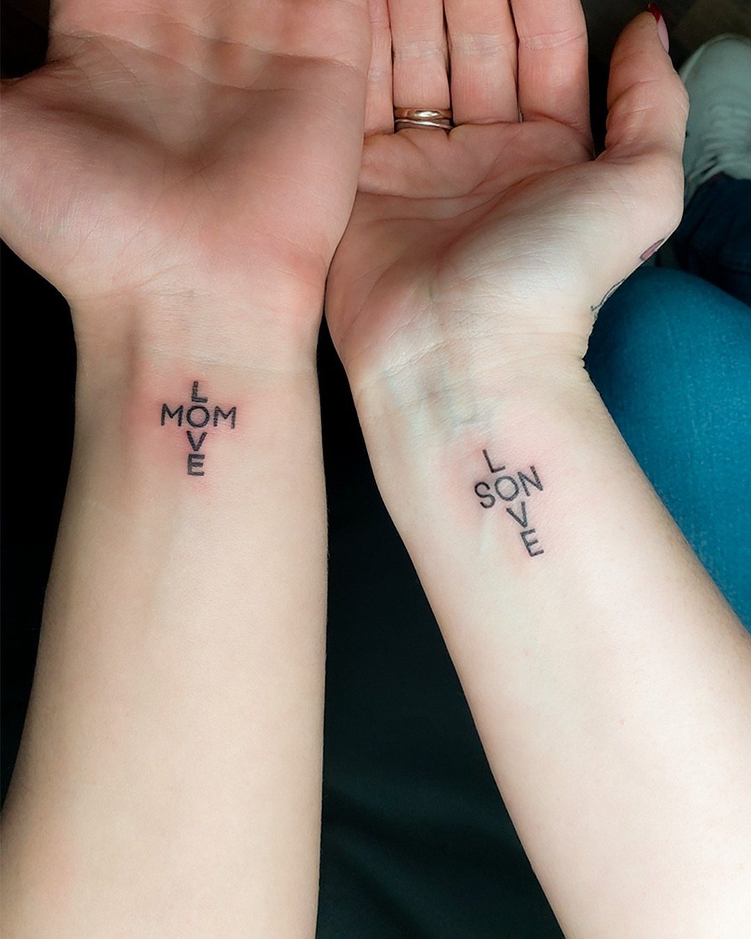 Two wrists with matching cross-shaped tattoos reading Love Mom and Love Son.