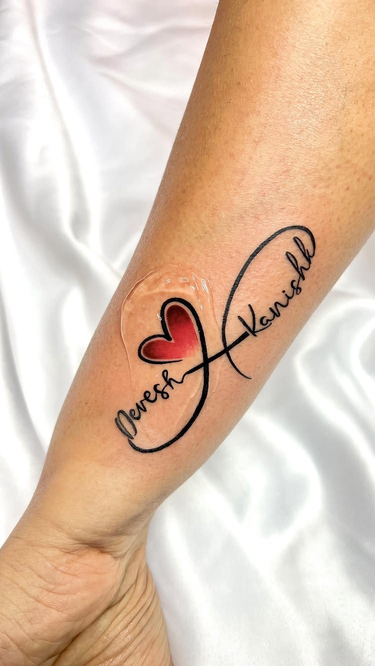 Infinity symbol tattoo on forearm with names Devesh and Kanishk and a red heart.